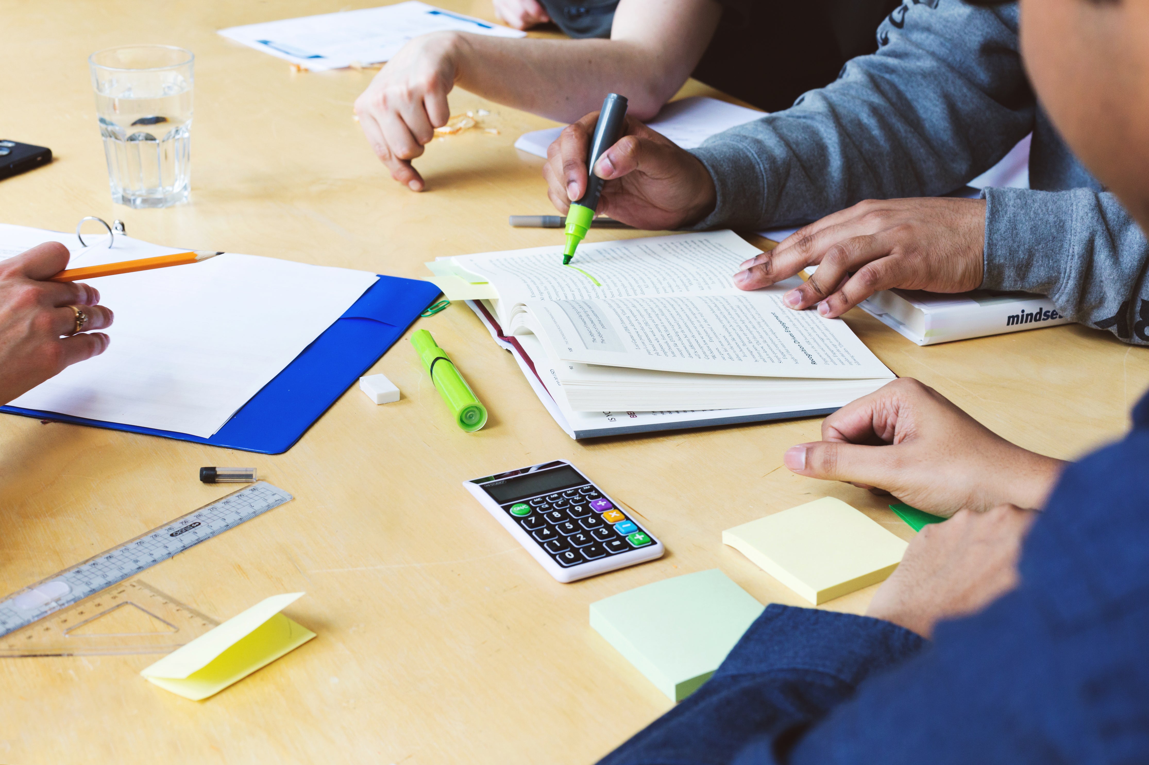 Work team meeting at table with books, highlighters, ruler, and calculator.